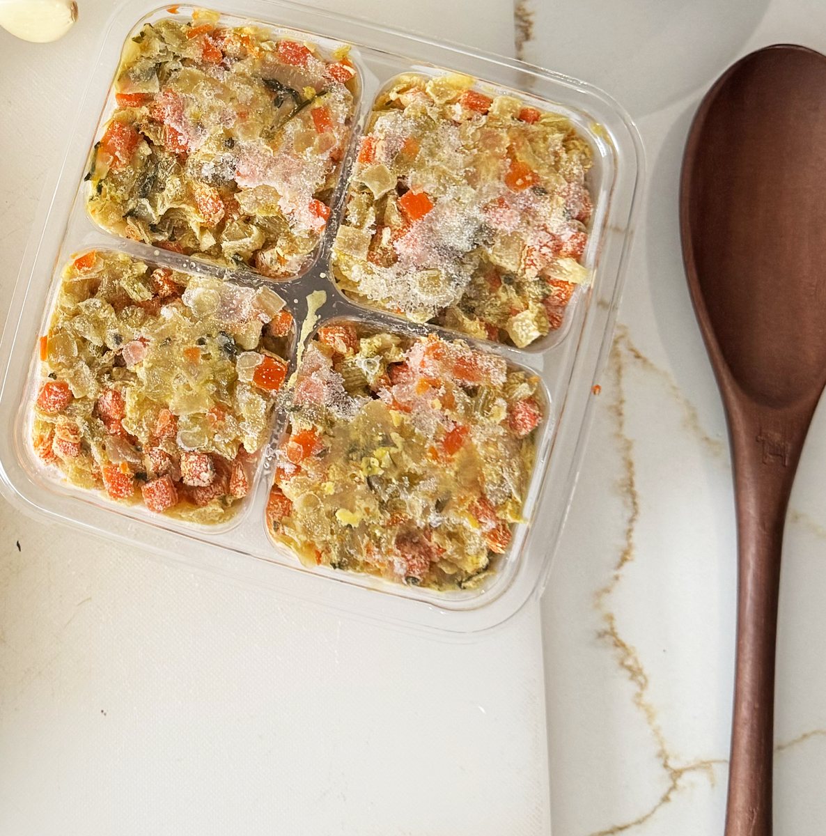 An opened pack showing four separate frozen 3 oz segments of mirepoix beside a wooden spoon